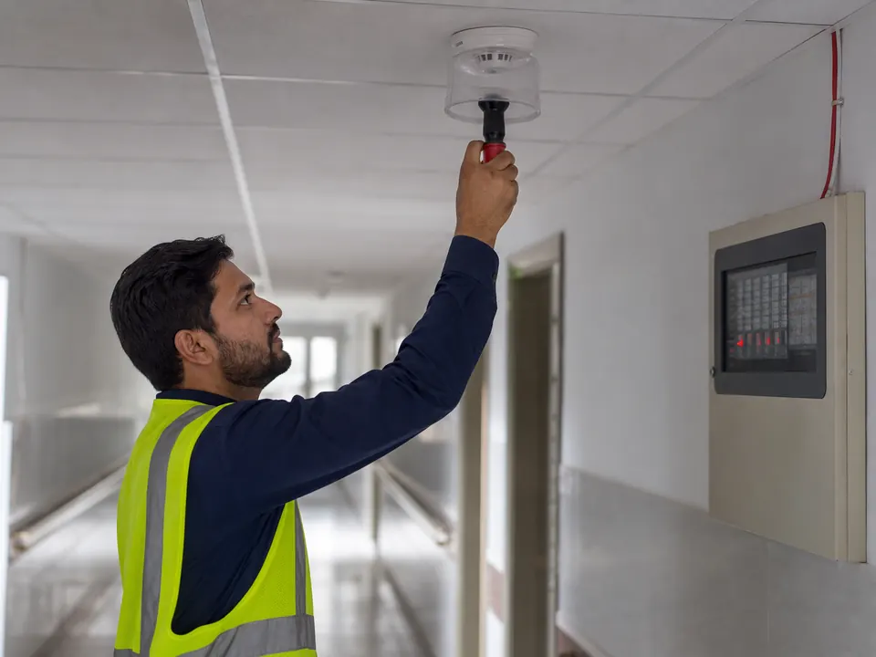 Technician testing a smoke detector in a clinic corridor